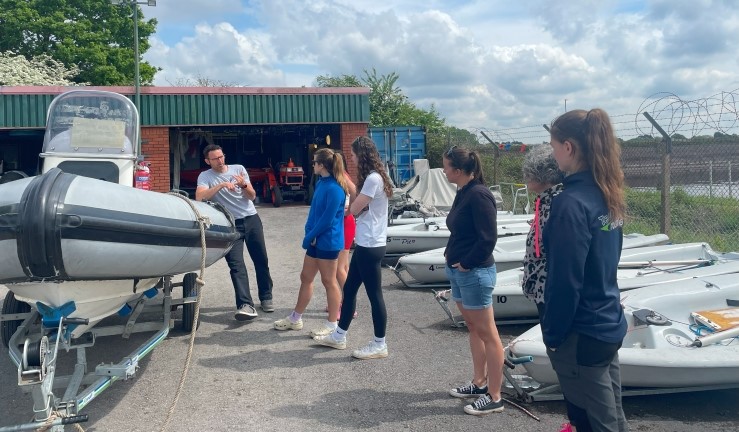 Half a dozen women gathered around a grey RIB and in instructor on shore as part of an RYA Powerboat Instructor Course. 