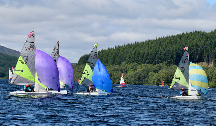 three young sailors competing in the RYA Scotland youth and junior championships each in their own white dinghy with neon green sails with purple blue and light blue jib sheets.