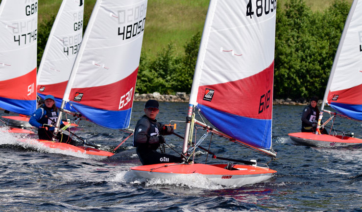 3 young sailors competing in the RYA Scotland youth and junior championships each in their own red and white dinghy.
