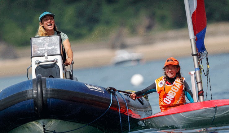 Girl laughing driving a safety boat with a young sailor smiling and holding the side