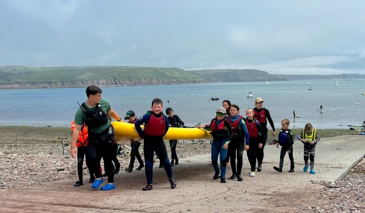 Regatta Fleet sailors working together to carry a giant SUP yellow up the slipway at Dale at Welsh Regional Junior Championships 2024.