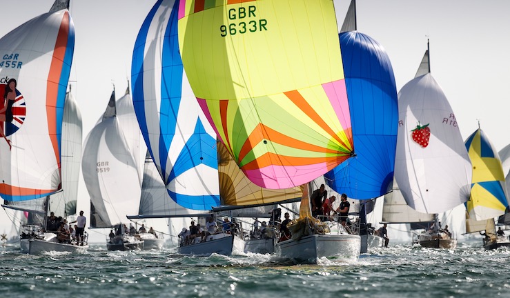 Lots of yachts racing downwind with colourful spinnakers flying on a sunny day.