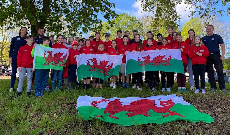40-strong team of young Welsh sailors wearing red team kit flanked by coaches and holding up Welsh flags at the Eric Twiname Junior Championships 2024.