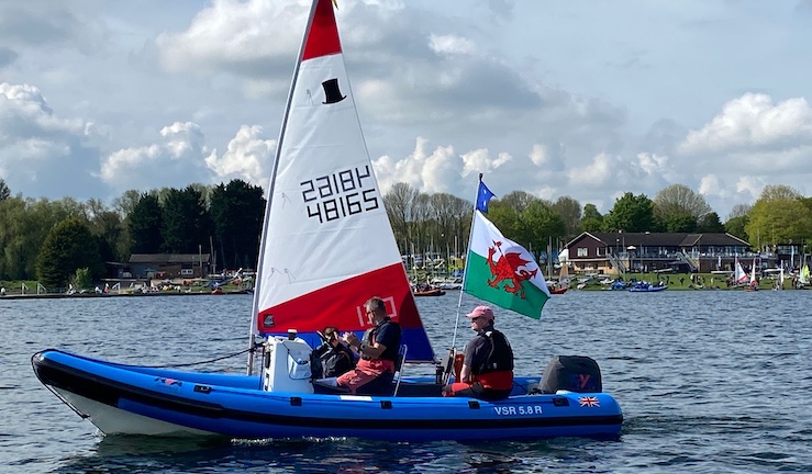 Blue RIB coach boat with two people aboard and flying a Welsh flag alongside a Topper dinghy with Rutland SC in the background at the Eric Twiname Championships 2024.
