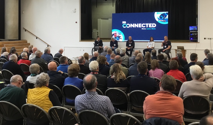 Conference room with lots of people seated and five people on stage with an RYA Connected blue screen behind.