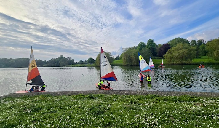 Junior Topper dinghies with red white and blue sails on the lake at Trimpley Sailing Club with green grass shoreline and blue skies.