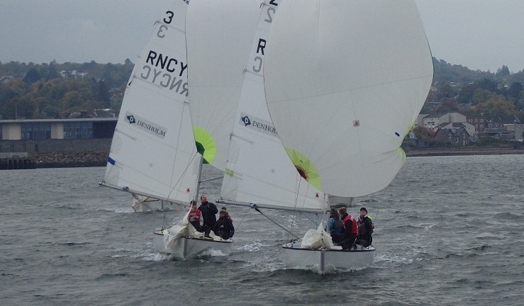 Two teams racing Sonar keelboats downwind on a grey day with white spinakers flying and shoreline in the background, Ceilidh Cup 2024 at Royal Northern & Clyde YC.