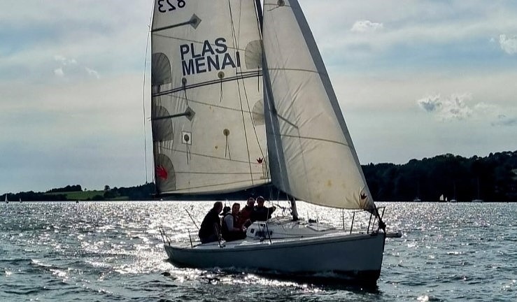 Keelboat sailing with the sun behind and sparking on the water, Plas Menai on the mainsail.