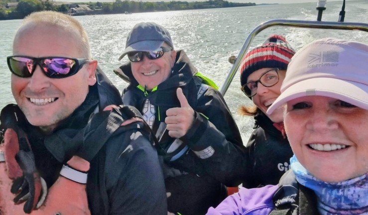 Group of four smiling people in selfie taken on a powerboat on the water at Plas Menai.