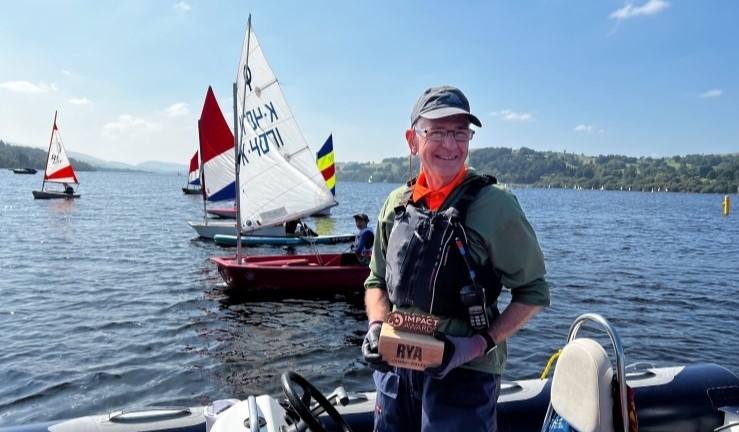 Paul Welsh smiling on receiving his Impact Award while on a RIB at Bala SC with junior boats sailing in the background.