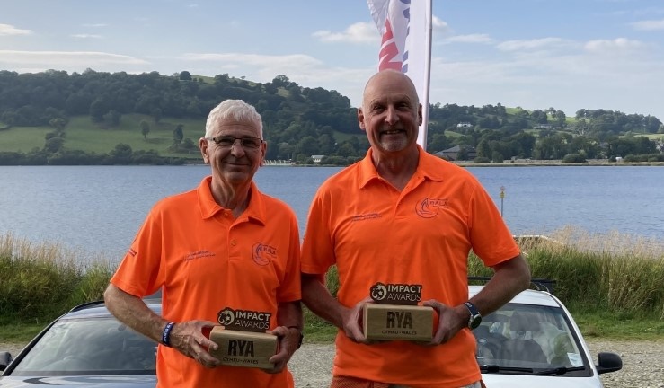 Volunteer instructors Paul Welsh and Mick Flemming in orange branded Bala Sailing Club polo shirts smiling with their RYA CW Impact Awards.