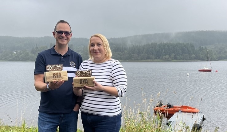 Andrew and Amanda Williams from Merthyr Tydfil SC with their RYA Cymru Wales Impact Awards outside at the club with the lake in the background.