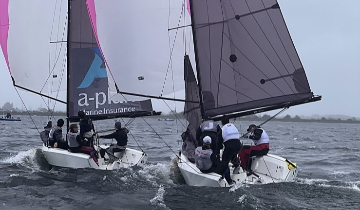 Two teams match racing RS21 keelboats downwind with spinnakers flying in big beeze and grey skies at the RYA National Match Racing Championship Grand Finals 2024.