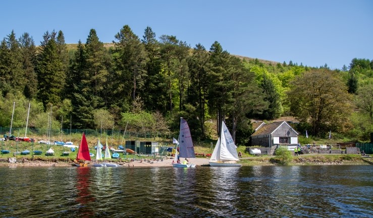 View over the water to Merthyr Tydfil SC on a sunny day with blue skies and sailing dinghies on the shoreline.