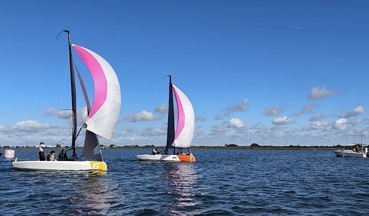 Two teams match racing RS21 keelboats downwind with white and pink spinnakers flying on a sunny day at Queen Mary SC, 2024 RYA Match Racing Series.