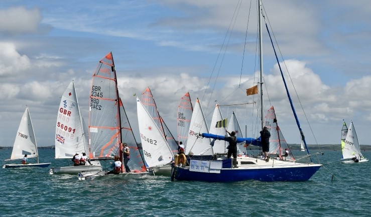 Mixed fleet of youth boats lining up alongside a committee boat for the start of a race at the Welsh Regional Junior Championships 2024.