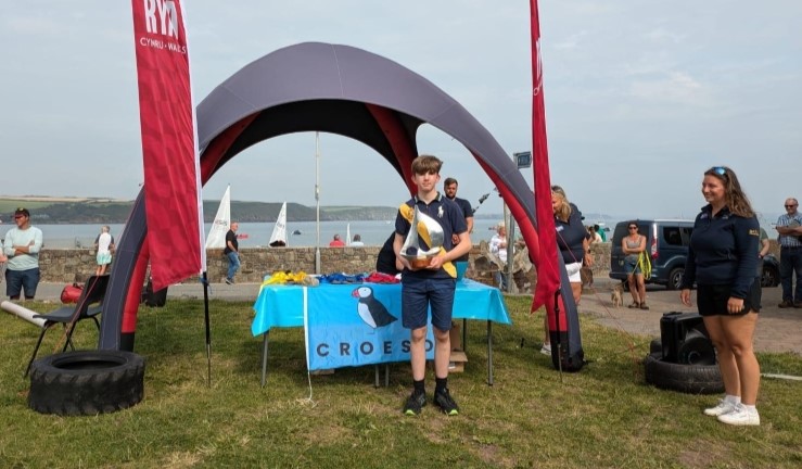 A young sailor presented with a large trophy at the CW OnBoard Festival prizegiving, Dale, 2024.