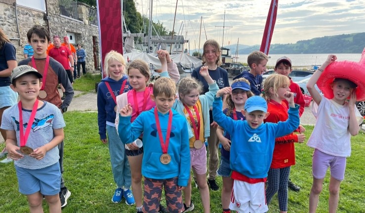 Smiley group of young sailors on shore with medals after taking part in the RYA CW OnBoard Festival at Bala, 2024.