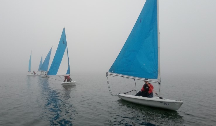 Five training boats with blue sails in a row on a misty day at Covenham Sailing Club.