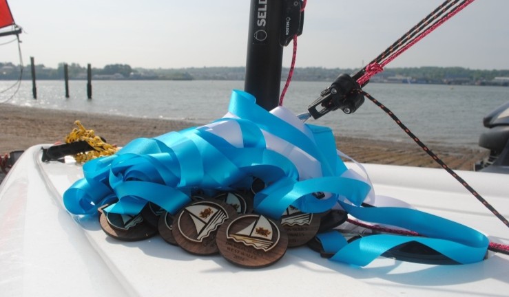 Dragon Series wooden medals with blue ribbons on the deck of a boat on a beach.