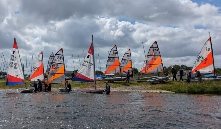Variety of youth and junior boats with colourful sails launching for a Dragon Series event.