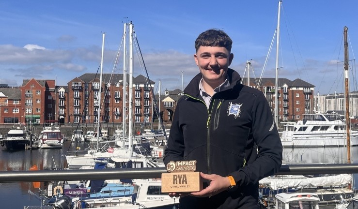 Aston Grindrod of Swansea Watersports with his RYA Cymru Wales Impact Award on a sunny day beside a marina.