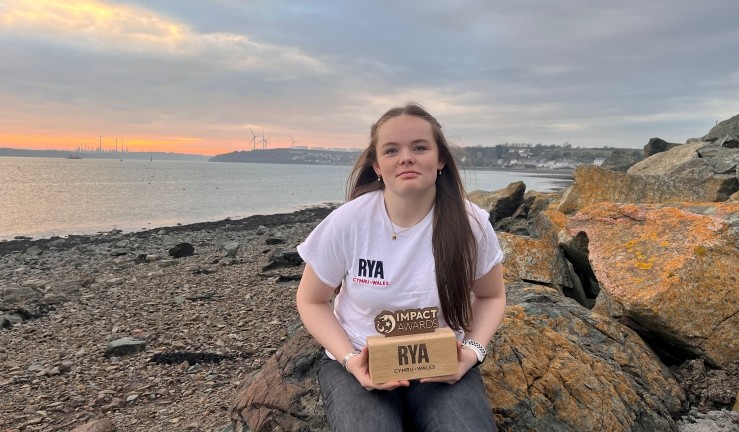 RYA Impact Award recipient Keira with her award on the shoreline.