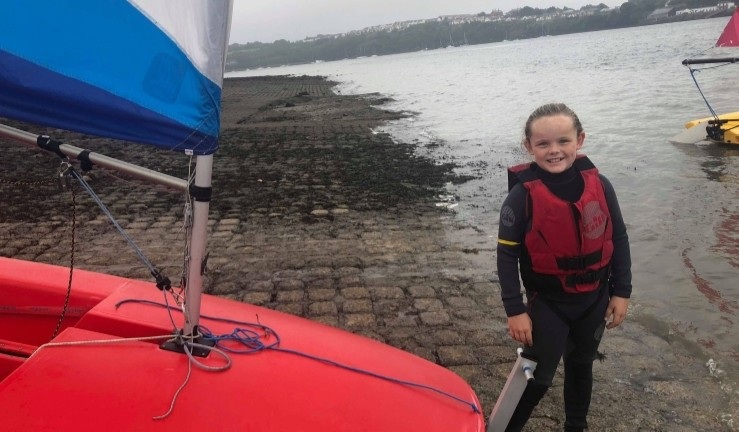 RYA CW Impact Awardee Keira aged just 8 and standing by a Topper on shore at her first ever taster session for sailing.