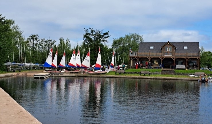 View of Llangorse SC's clubhouse from the pontoon/water with Topper sails up on shore.