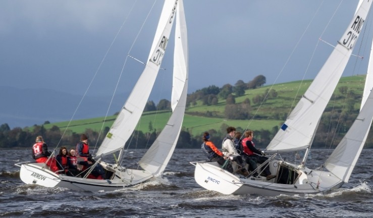 Two teams match racing Sonar keelboats at the Ceilidh Cup in Scotland with grey sky and green hills.