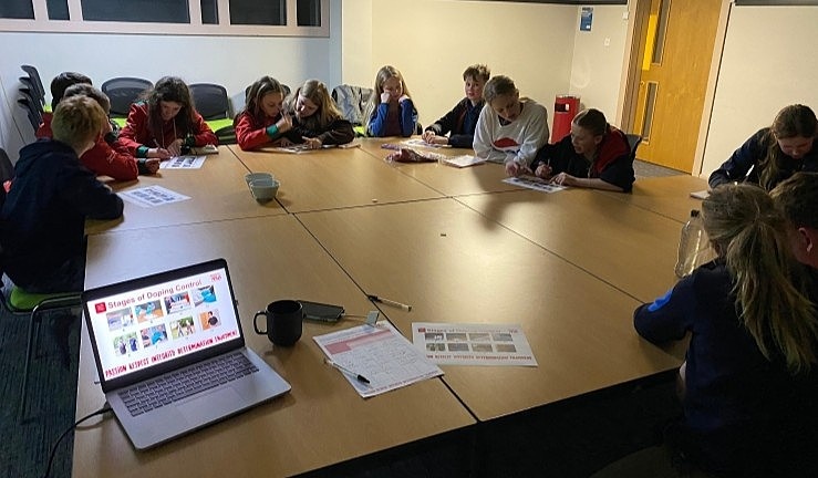 Group of RYA Cymru Wales squad sailors around the table at a training camp to learn about Anti-Doping rules, with laptop open showing clean sport resources in the foreground.