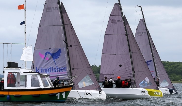 Three teams racing RS21 keelboats off the startline with the Rutland Sailing Club committee boat at the starboard end.