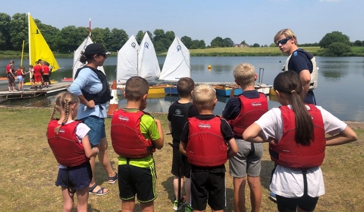 Half a dozen children gathered around on shore listening to an instructor at an All Afloat day hosted by Gresford SC.