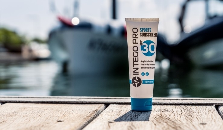 Intego Pro sunscreen on a waterside wooden deck in the sunshine with moored boats in the background.