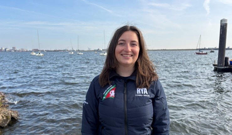 Photo of RYA Cymru Wales' new Pathway & Events Officer Hatty Morsley standing by the sea on a sunny day.