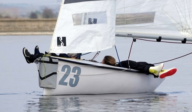 Two sailors lying down and relaxing with feet over the side of a Firefly dinghy in no wind at the RYA/UKTRA National Team Racing Championship 2025. 