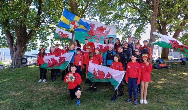 Welsh sailors at the Eric Twiname Junior Championships on shore waving national flags.
