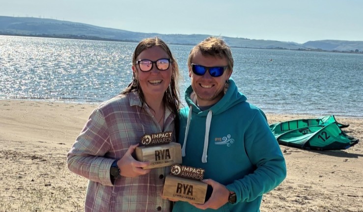 Kate and Dan Stevens on the beach at Dovey on a sunny day with their Impact Awards.