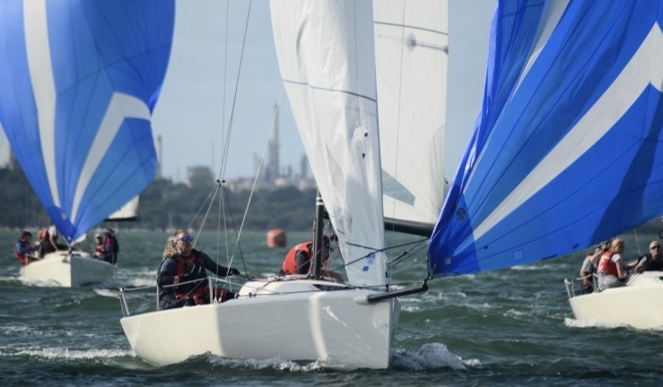 British Keelboat League action with teams aboard J70s battling it out downwind sailing towards the camera with blue and white spinnakers flying.