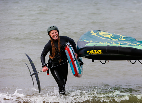 Woman carrying wing and foiling board out of sea