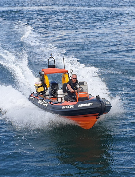 Orange rescue rib at sea. Man at helm wearing dark clothing and sunglasses