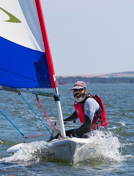 Man with beard and wearing cap sailing small dinghy 