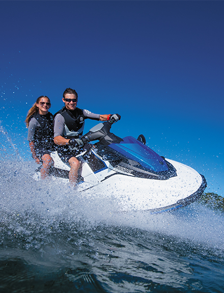 Man and woman smiling riding a personal watercraft pw on a sunny day with blue sky