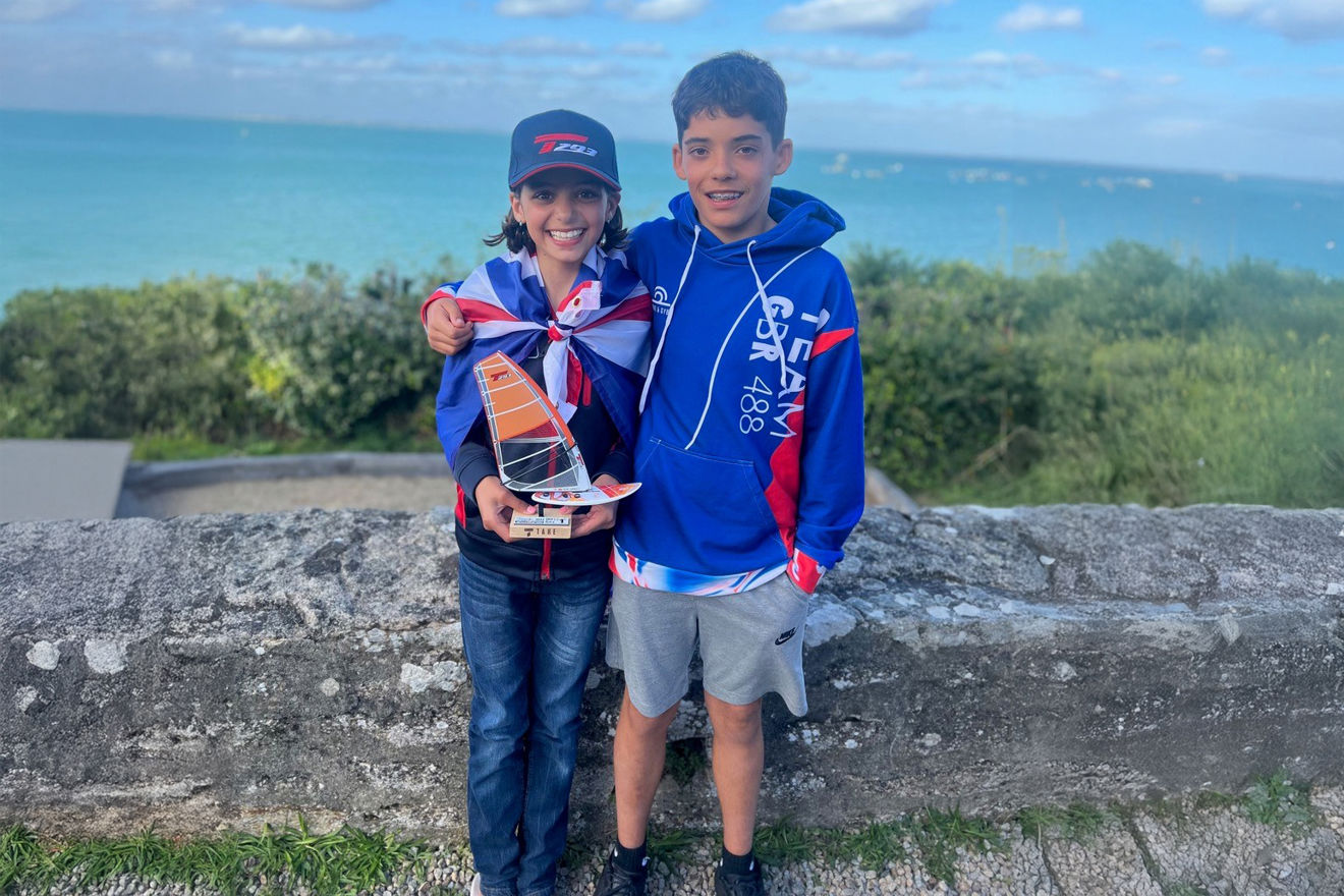 Two young children stood infront of the water showing their awards