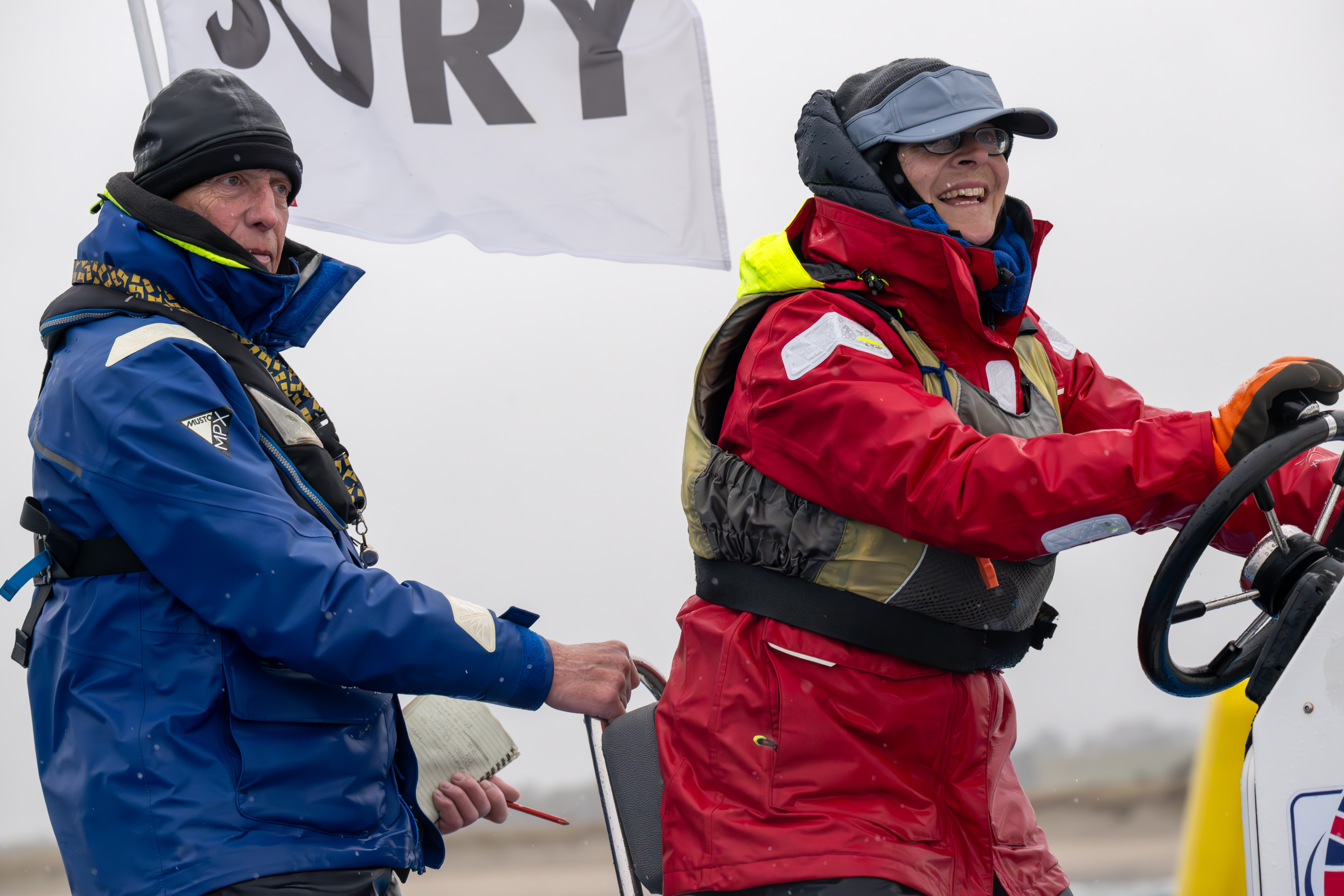 Mid shot of two sailors on boat, one is smiling and the other is concentrating