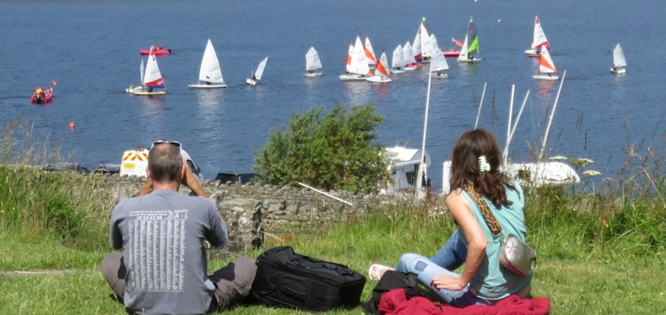 Couple sitting on a hill watching dinghies sailing at Teesdale