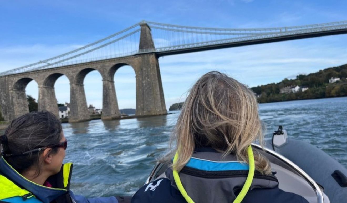 Blue skies and water with two people driving a powerboat towards the Menai Strait bridge at the Big Weekend 2024.