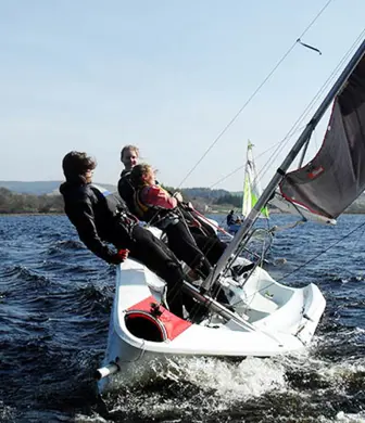 Two people leaning out (hiking) of a sail boat to help steer it
