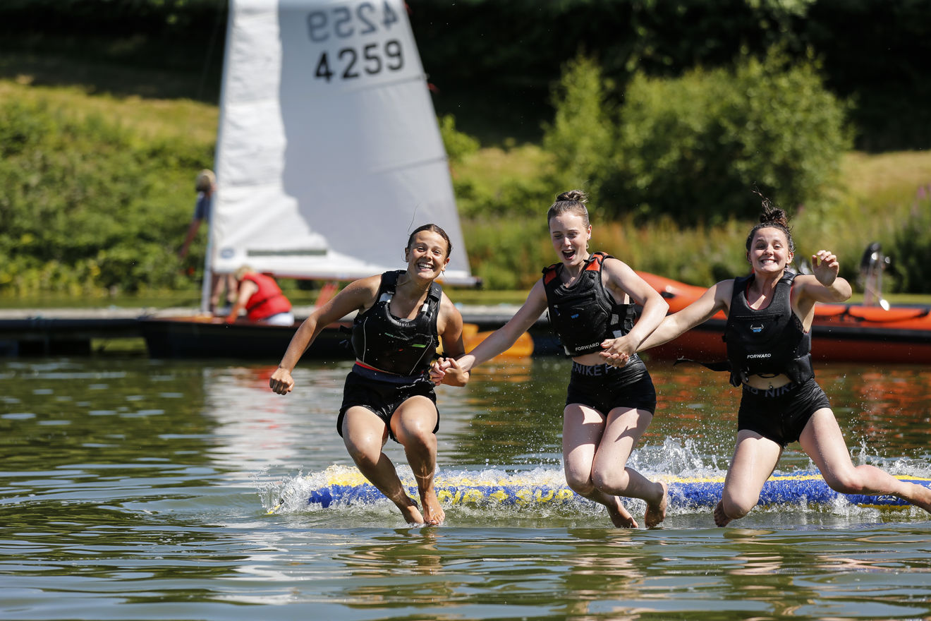 three girls jumping in the lake all smiling