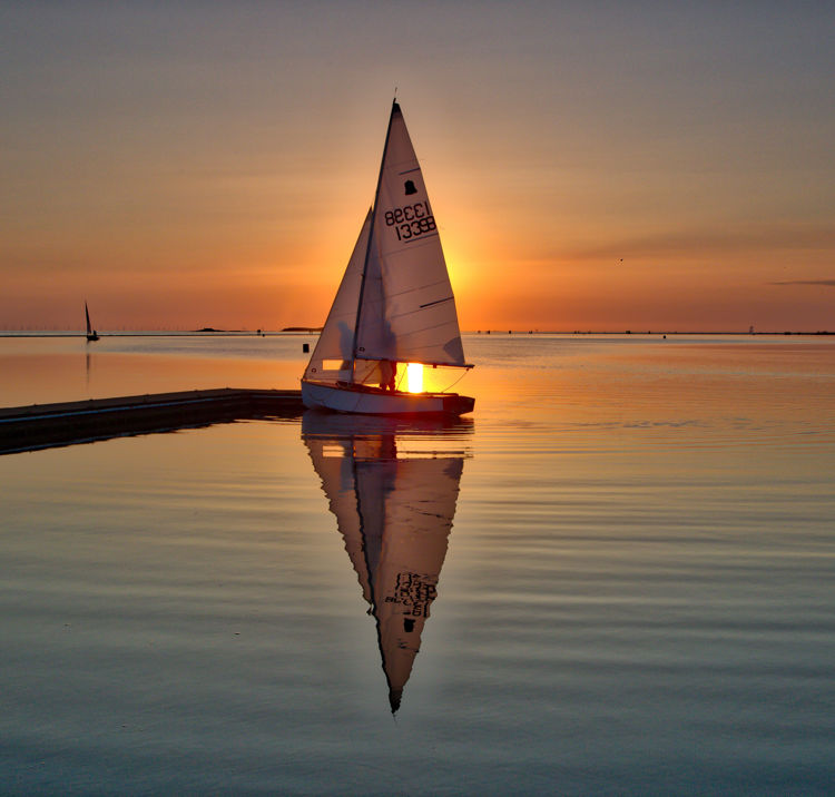 Single sailboat in calm waters at sunset